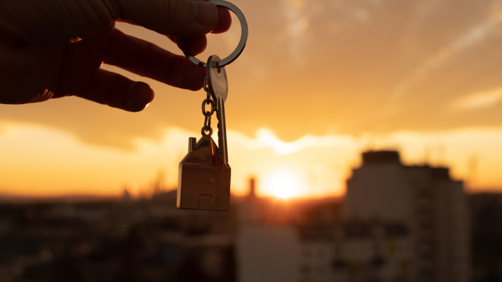 Hand holding keys with a sunset over a city skyline in the background